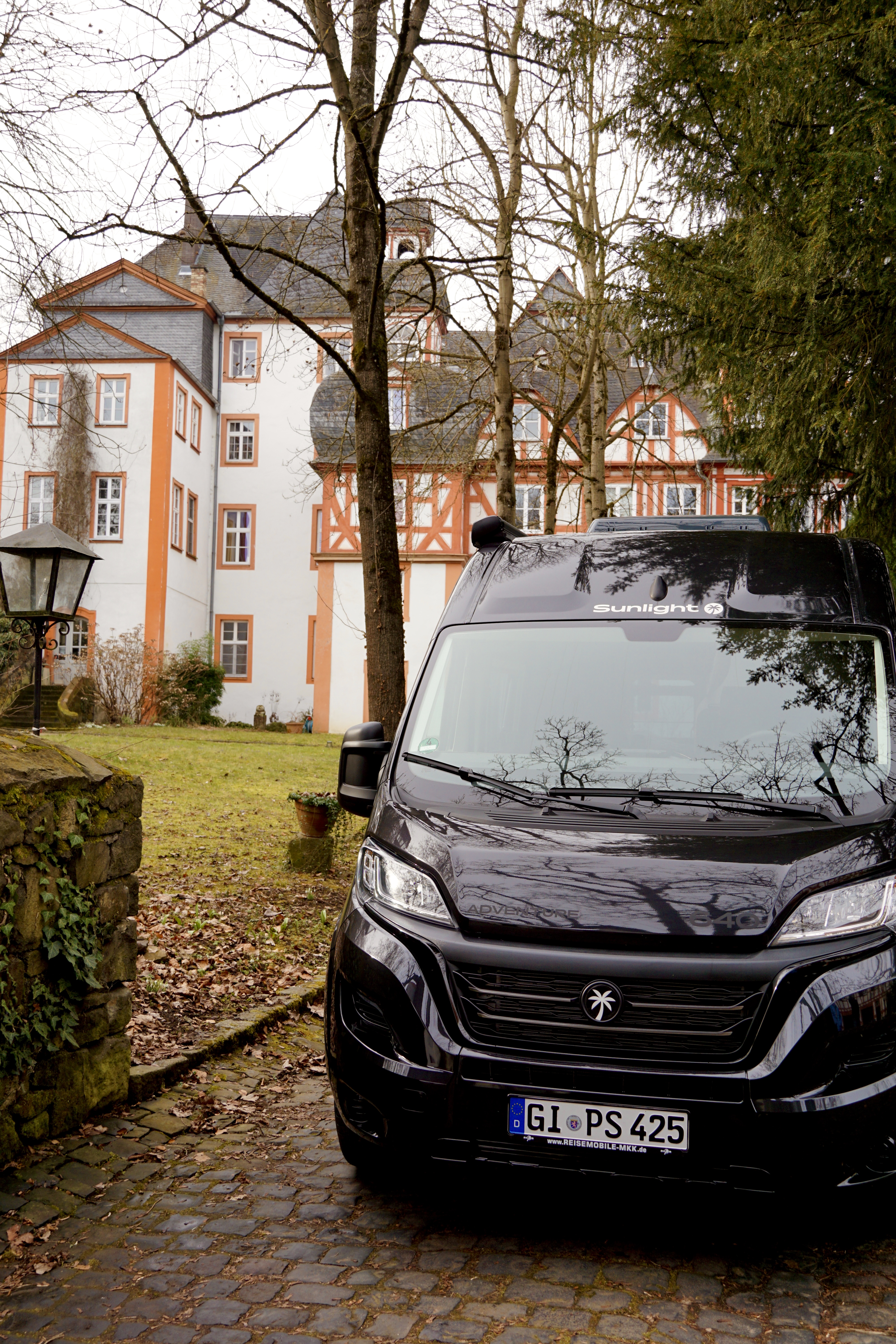 Schwarzer Campervan von Fiat in der Natur vor einem Schloss
